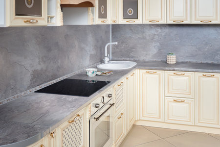 Interior of modern beige classic style kitchen with golden elements with built-in appliances electric induction hob stove cooker with ceramic top surface electric oven stone sink and extractor fan.の写真素材