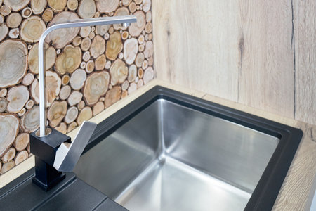 Modern design chrome rectangular section water tap closeup over stainless steel sink on table top made of natural wooden kitchen apron decorated with wall cross section of tree trunks cut tree logsの写真素材