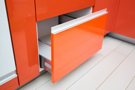 Upscale Maple Red kitchen drawer for plates or dishes shelf cabinet. Pull out rack cabinet filler pantry near oven. Horizontal drawer shelf with orange front wooden panel half opened side view.の写真素材