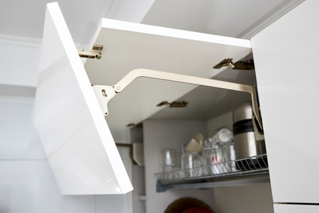 Part of contemporary kitchen interior. Opened White horizontal Kitchen Cabinet with Plates and Glasses on Shelf. Kitchen cabinet door lifting mechanism.の写真素材