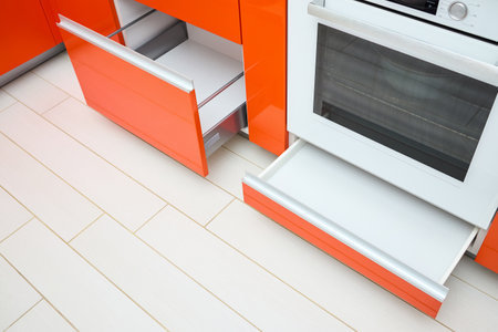 Upscale Maple Red kitchen two drawer for plates or dishes shelf cabinets. Pull out rack cabinets fillers pantry under and near oven. Horizontal drawers shelf with orange front wooden panel side view.の写真素材