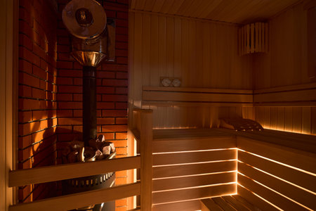 Russian sauna bathhouse with muted intimate light from under the bottom of bench wooden lantern hygrometer thermometer with sauna stove oven with internal stone heater and stones and chimney or pipe.の写真素材
