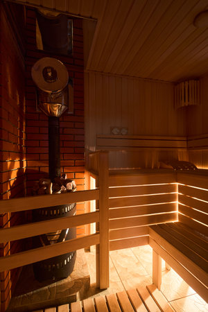 Russian sauna bathhouse with muted intimate light from under the bottom of bench wooden lantern hygrometer thermometer with sauna stove oven with internal stone heater and stones chimney vertical.の写真素材