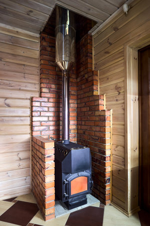 Rural home interior element. Cast iron steel wood stove burning warm on floor tile inside brick fireplace, with carbon monoxide smoke detector.の写真素材