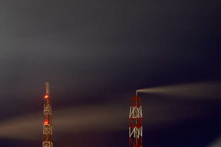 Signaled with red lights smoke pipes of petrochemical plant at night dark dramatic sky long time exposure shot with copyspace. Concept of environment pollution greenhouse effect global warmingの写真素材
