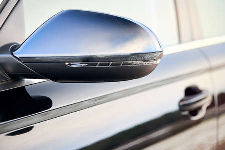 Luxury car parts. Black side driver car exterior mirror with turn signal repeater closeup selective focus with sky and clouds reflection and copyspace.の写真素材