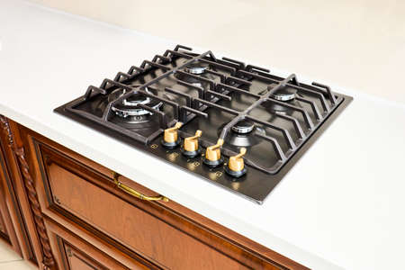 Modern gas hob stove made of steel and cast iron with golden controls using natural gas or propane for cooking products on light countertop in kitchen interior.の写真素材