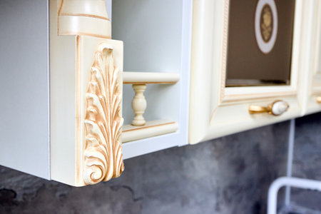 Selective focus fragment of beige wooden cabinetry kitchen carved detail. Carved decorative detail. Wooden pilasters. Decor furniture. Carved decor elements. Decorative elements.の写真素材
