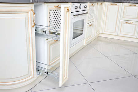 Pull out spice rack cabinet filler pantry. Interior of modern kitchen in classic style with golden elements in beige colors. Vertical drawer for spices shelf under countertop with front wooden panel.の写真素材