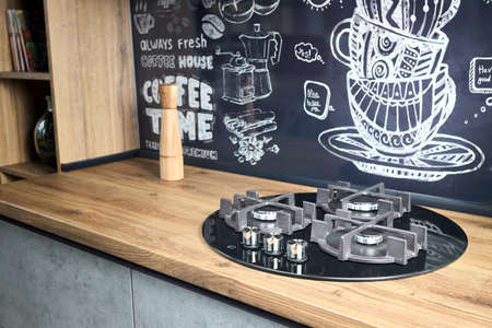 Modern kitchen equipment concept black tempered glass round shape gas hob with cast-iron grill with three gas burners on brushed oak counter top for convenient cooking on gas cooktop with pepper mill.の写真素材