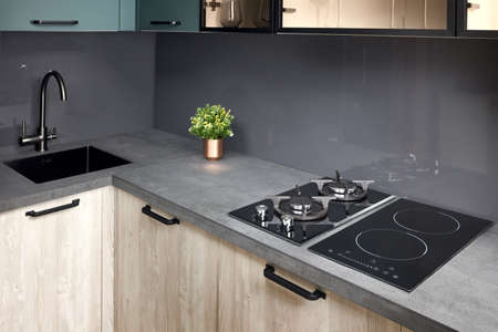 Upscale modern flat design Aqua Menthe kitchen in luxury home with induction electric hob flat oak or walnut wooden panels with flower in vase and sink with tap mixer of modern design.の写真素材