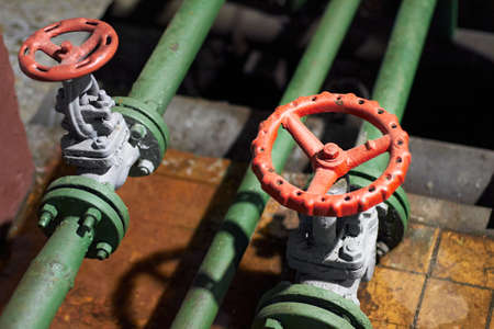 Two industrial chemical petrochemical retro style green valves closeup with selective focus on red steering wheel mounted with flange connection on green pipe, out of focus foreground with copyspace.の写真素材