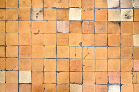 Orange brown white beige old shabby worn out floor tiles with damages cracks dirt caverns potholes and paint stains. Art design background texture.の写真素材