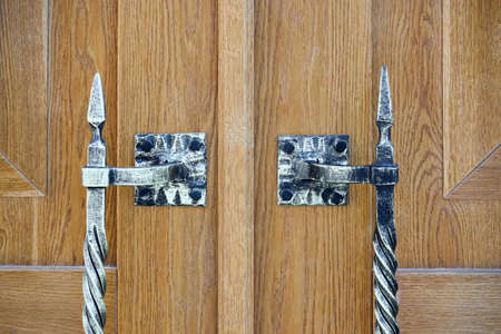 Forged patinated aged door handle twisted with pyramidal top form of pike or spear selective focus on brown old wooden door with copyspace, vertical shot.の写真素材
