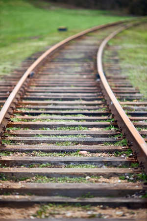 Selective focus rounding of railway abandoned rusty, overgrown with grass and moss. Empty turning single track of railways. Shallow focus perspective view of rounded rails bend vertical.の写真素材