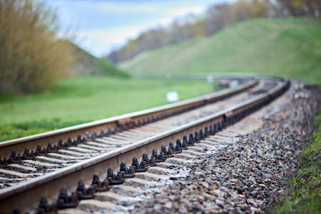 Selective focus railway track turns and twists between hills. Empty rounding and turning single track of railways. Shallow focus perspective view of rounded rails bend horizontal.の写真素材