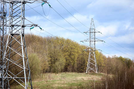 High voltage electric high voltage electric transmission power tower with electric glass insulator of over cloudy stormy dark sky near spring forest.の写真素材