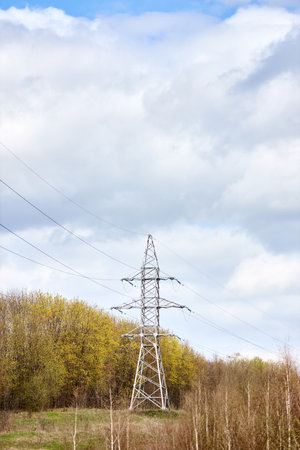 High voltage electric high voltage electric transmission power tower with electric glass insulator of over cloudy stormy dark sky near spring forest. Vertical shot.の写真素材