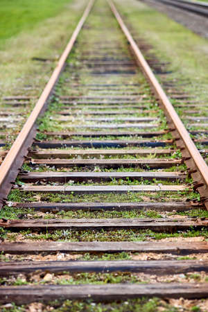 Selective focus on going straight railway abandoned rusty, overgrown with grass and moss. Empty turning single track of railways. Shallow focus perspective view of foing ahaid rails vertical.の写真素材