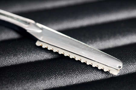 Barbershop tool. Selective focus, part of barber thinning razor layer, hair trimming, cutting comb and neck-cut blade over dark waved artificial leather background with copyspace.の写真素材