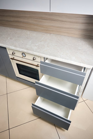 Solution for placing kitchen utensils in modern kitchen. Horizontal sliding pullout drawer shelves storage in cupboard for kitchenware under porcelain stoneware countertop with copyspace vertical.の写真素材