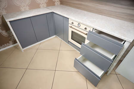 Solution for placing kitchen utensils in modern kitchen. Horizontal sliding pullout drawer shelves storage in cupboard for kitchenware under porcelain stoneware countertop with copyspace horizontal.の写真素材