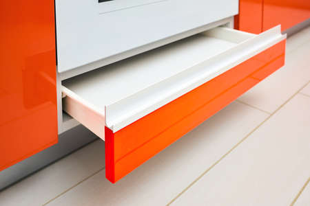 Drawer under oven. Maple Red kitchen drawer for plates or dishes shelf cabinet under oven. Selective focus Pull out rack cabinet filler pantry. Horizontal drawer with orange front wooden panel.の写真素材