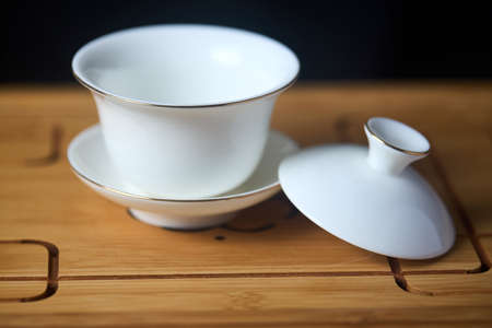 Gaiwan on chaban selective focus. Tea ceremony gong fu cha. Chinese white pottery Dehua white Chinese porcelain gaiwan bowl tea cup and lid with gold border on bamboo teaboard tea tray or chaban.の写真素材