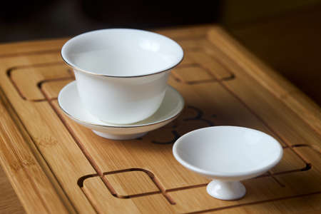 Gaiwan on chaban selective focus. Tea ceremony gong fu cha. Chinese white pottery Dehua white Chinese porcelain gaiwan bowl tea cup and lid plate with gold border on bamboo teaboard tea tray chabanの写真素材