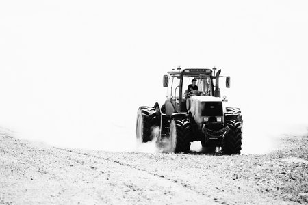 Grodno - April 2021: Agricultural industry tractor cultivation in field in clouds of dust high contrast black and white image. Selective focus farm tractor with plow with copyspace.のeditorial素材