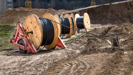 Cable high voltage electric in roll or round coil on ground. Concept of electricity supply for construction projects. Several wooden coils with power cable laid in trench 16x9 image.の写真素材