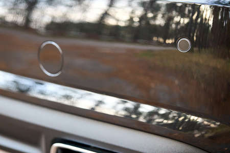 Selective focus on rear bumper parking sensors near exhaust pipe at back of luxurious car bumper close up with forest and sky reflections with copyspace.の写真素材