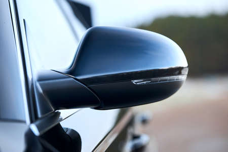 Luxury Black car parts left side driver car exterior mirror with turn signal repeater closeup selective focus with sky and clouds reflection, copyspace.の写真素材
