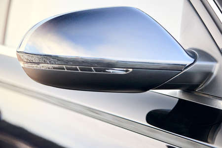 Luxury Black car parts right side driver car exterior mirror with turn signal repeater closeup selective focus with sky and clouds reflection, copyspace.の写真素材