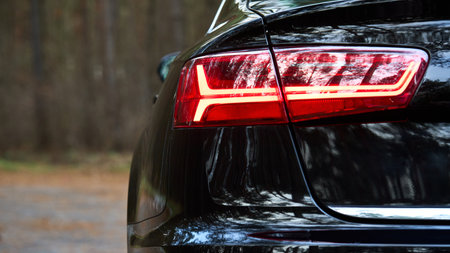 GRODNO, BELARUS - DECEMBER 2019: Audi A6 4G, C7 2016 Left back led modern rear light or taillight of black metallic car shot closeup selective focus on out of focus forest background with copyspace.のeditorial素材