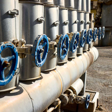 Blue industrial handwheels of valves in a row on petrochemical plant pipelines of steam and heating water supply system selective focus over out of focus background square shot.の写真素材
