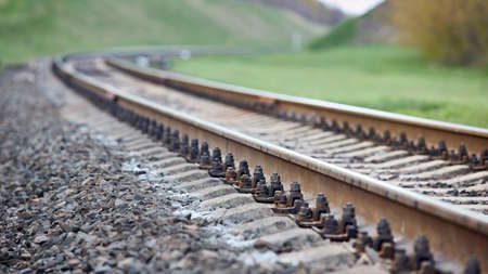 Selective focus railway track turns and twists between out of focus hills background. Empty rounding and turning single track of railways. Shallow focus perspective of rounded rails bend horizontal.の写真素材