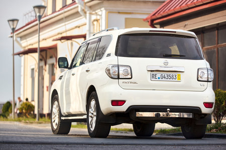 Berlin - October 2021: white metallic SUV japanese 4x4 car Nissan Patrol 6th Sixth generation Y62 V8 with trailer device parking sensors parked at sunny old european street back view with copyspace.のeditorial素材