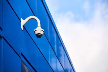Panoramic adaptive dome CCTV camera with IR illuminators and artificial intelligence for wide area coverage and mega zoom mounted on blue aluminum composite panels facade of commercial building.の写真素材