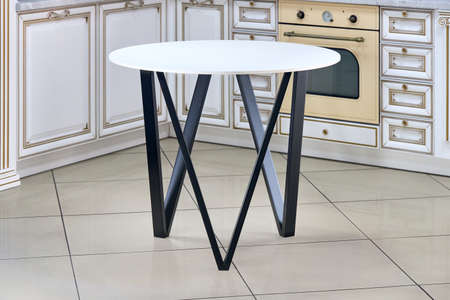 Loft-style kitchen table with round light stoneware countertop and black squared rectangular steel legs with out of focus kitchen on background.の写真素材