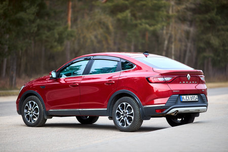 Berlin - March 2022: 2021 Renault Arkana e-Tech hybrid SUV car three fourth left side back view outdoors parked on street near forest.のeditorial素材
