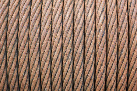 Steel cable sling hoist. Old obsolete rusty steel braided cable wounded on drum of industrial winch selective focuse macro closeup texture background.の写真素材