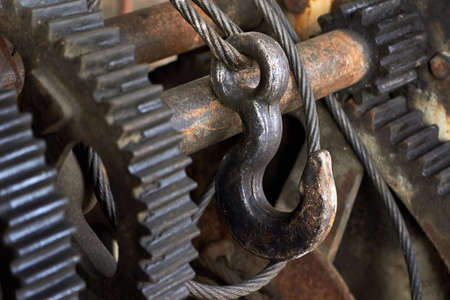 Steel cable sling hoist hook with gears. Wire rope sling and crawler drum of lifting crane machine. Closeup selective focus industrial mechanism detailing steampunk background.の写真素材