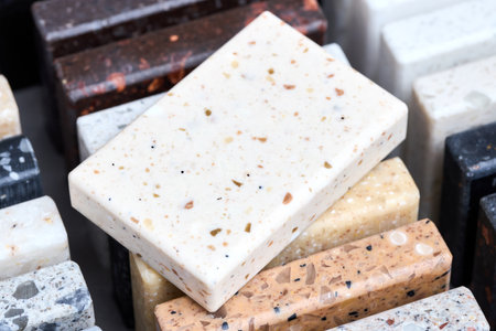 Porcelain one stoneware square sample laid on kitchen countertop examples of future kitchen fasade exterior. Samples slabs of natural granite marble quartz for stone countertops close up.の写真素材