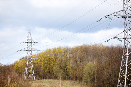 High voltage electric high voltage electric transmission power tower with electric glass insulator of over cloudy stormy dark sky near spring forest. Selective focus shot.の写真素材