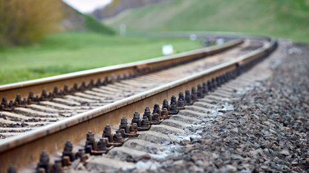 Selective focus railway track turns and twists between hills. Empty rounding and turning single track of railways. Shallow focus perspective view of rounded rails bend horizontal 16x9.の写真素材