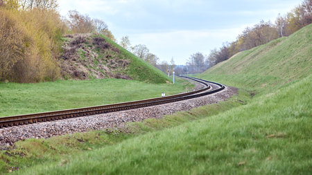 Selective focus railway track twists and turns between hills. Empty rounding and turning single track of railways. Shallow focus perspective view of rounded rails bend horizontal 16x9.の写真素材