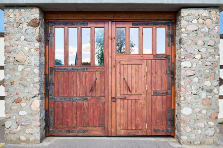 Old textured large hardwood doors, old brick wall with big vintage stable gates mates with forging with forged fitting elements. Wooden barn doorの写真素材