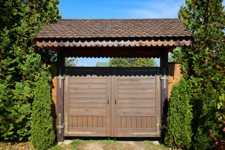 Old fashioned wooden gate with a tiled wooden roof canopy with forging with forged fitting elements and thuja hedge.の写真素材