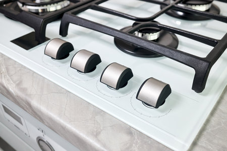 Hob cooker stove oven made of white glass grill stainless steel control knobs selective focus over out of focus oven with burner on countertop made of ceramic stoneware background.の写真素材